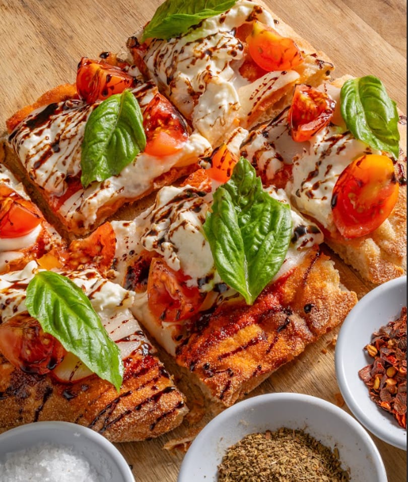 Close-up of a sliced flatbread pizza with tomatoes, mozzarella, basil, and balsamic glaze.